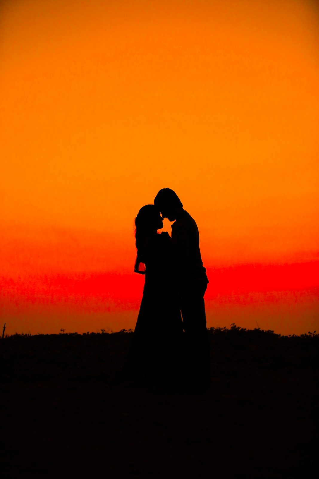 Silhouette of a couple embracing against a vivid sunset sky
